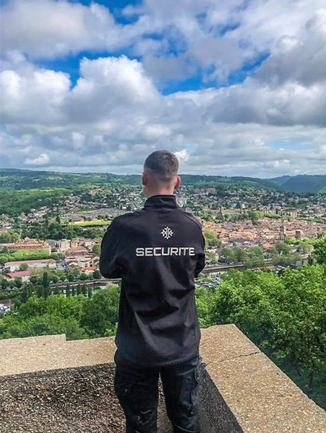 agent Pro Tech 12 surveillant Villefranche-de-Rouergue depuis une terrasse face au paysage urbain vallonné,