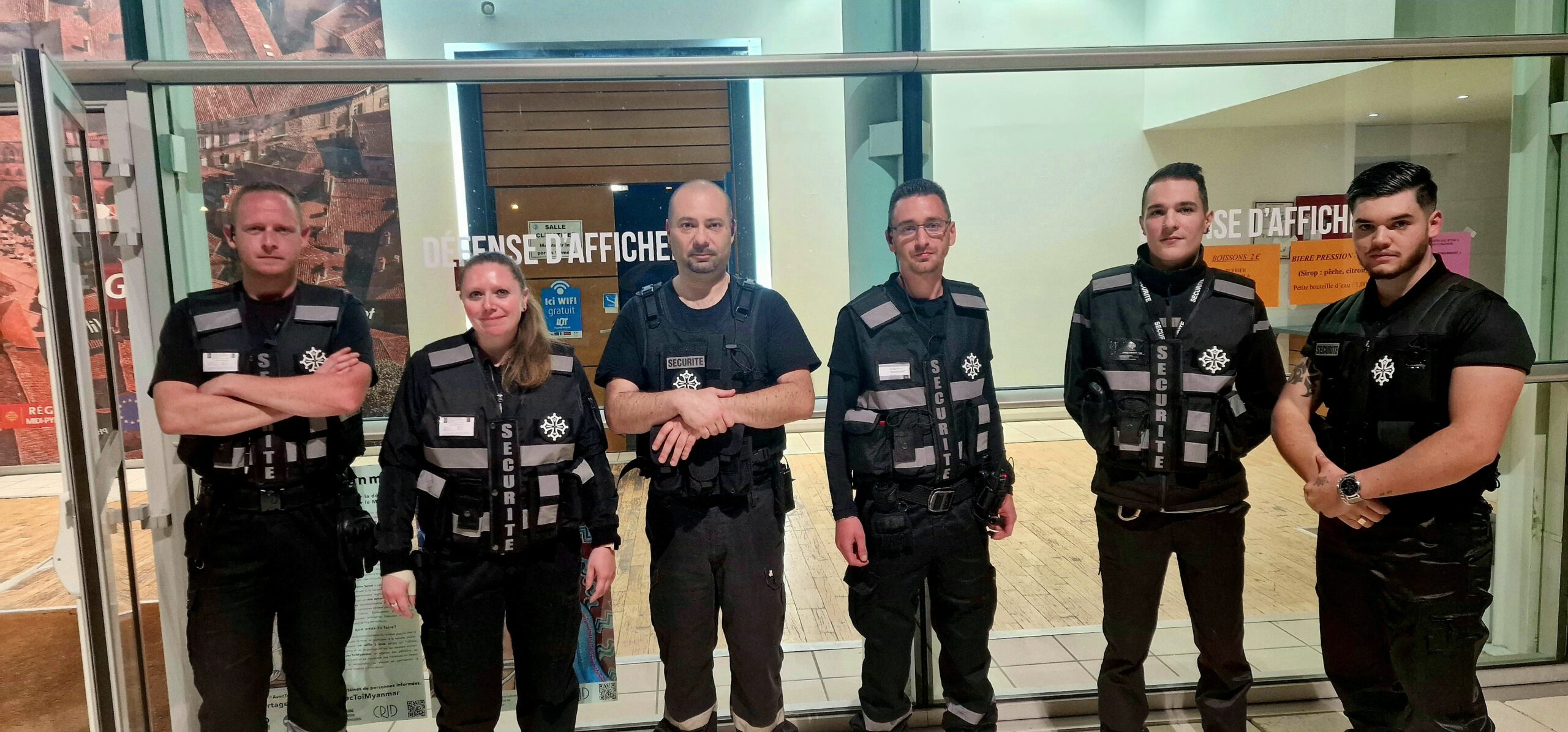 Équipe Pro Tech 12 en uniforme de sécurité à Villefranche-de-Rouergue devant une baie vitrée intérieure,