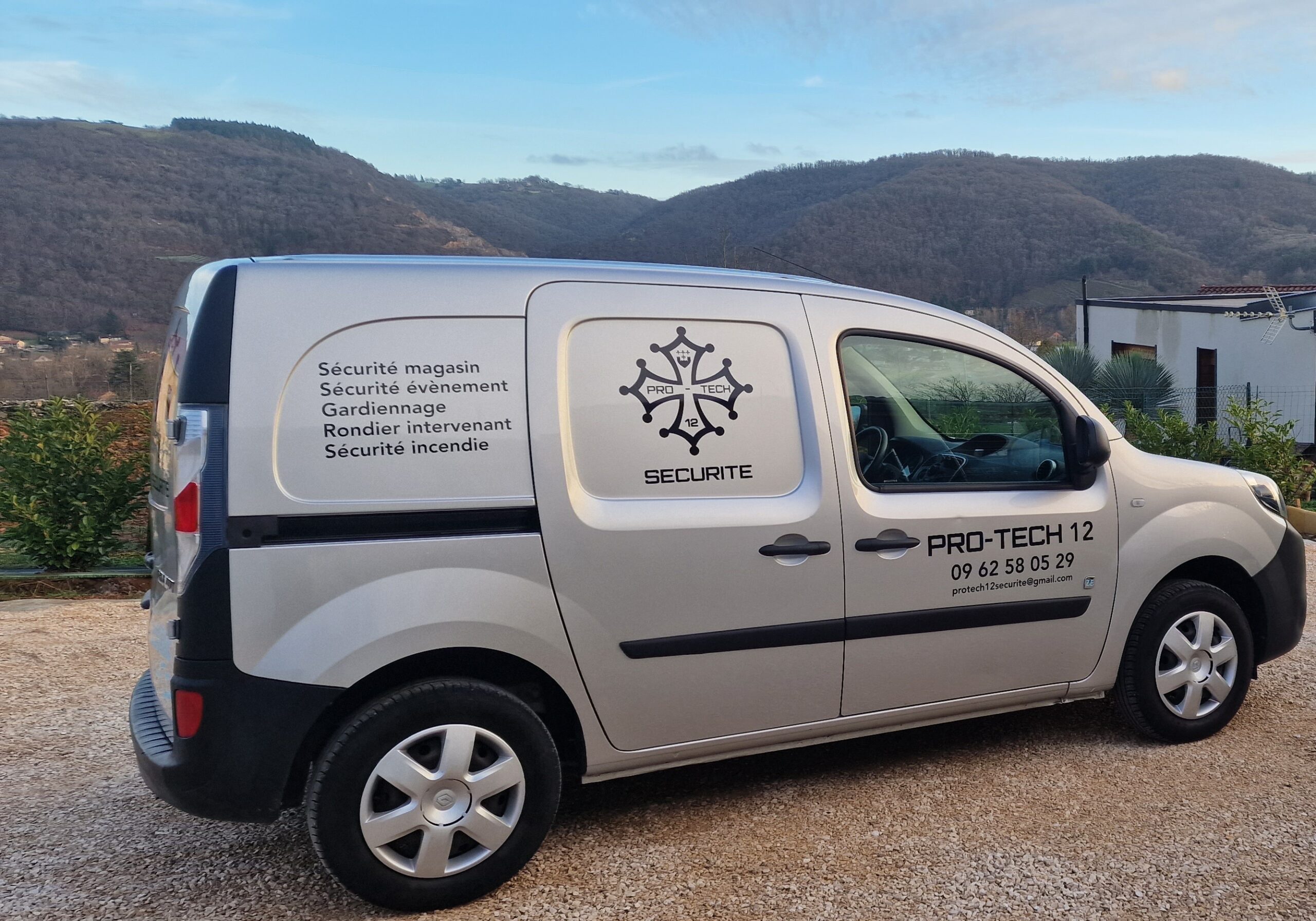 Utilitaire Pro Tech 12 sécurité stationné à Villefranche-de-Rouergue devant un paysage de campagne,