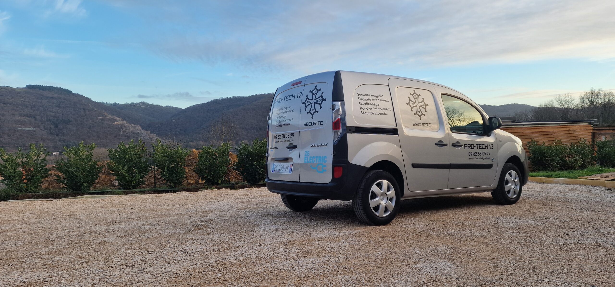 Camionnette Pro Tech 12 stationnée à Villefranche-de-Rouergue sur fond de collines verdoyantes,